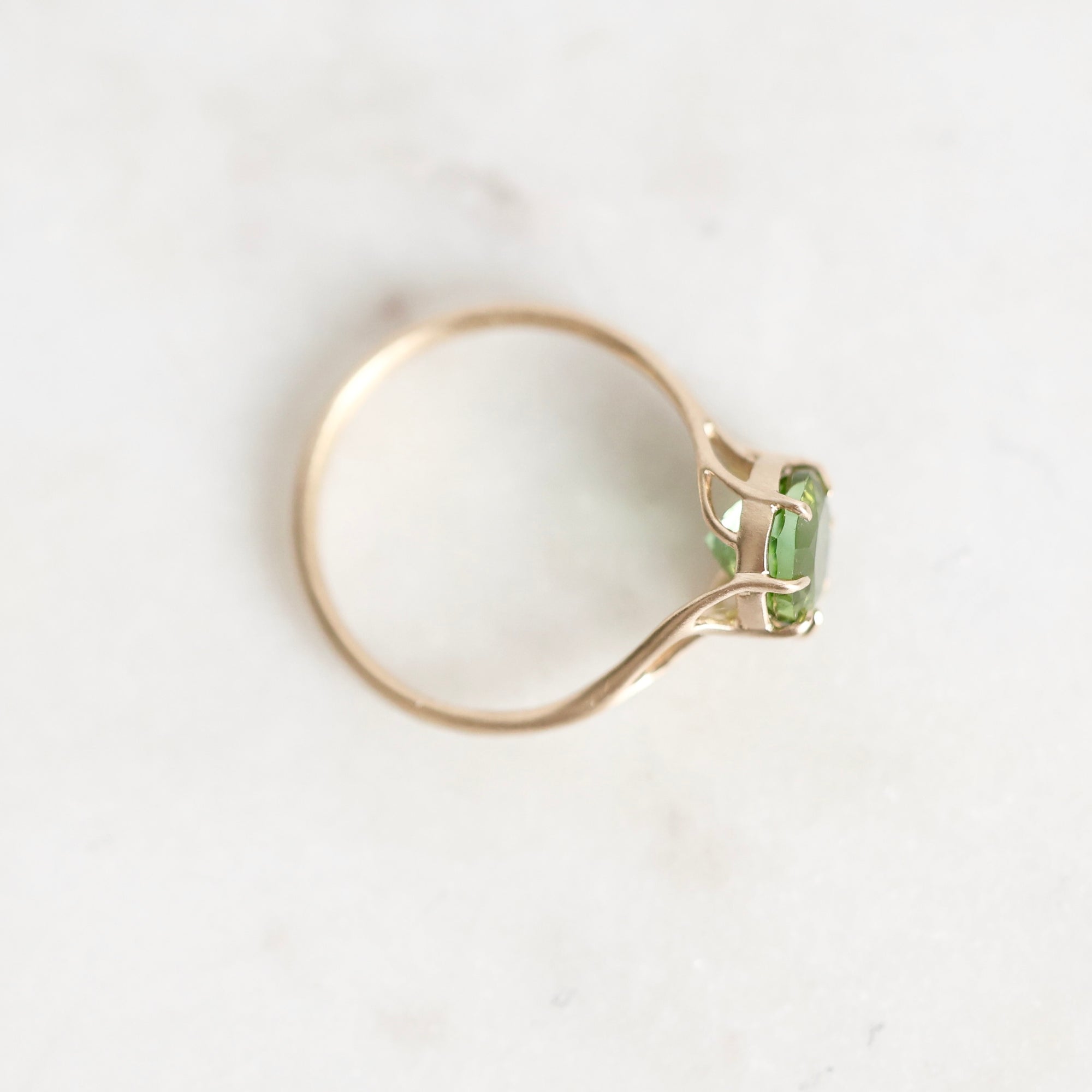 A gold ring with a small green rectangular gemstone, photographed on a light marble-like surface.