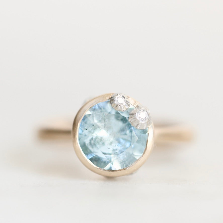 Light blue gemstone ring set in gold bezel accented with platinum barnacles set with diamonds. 