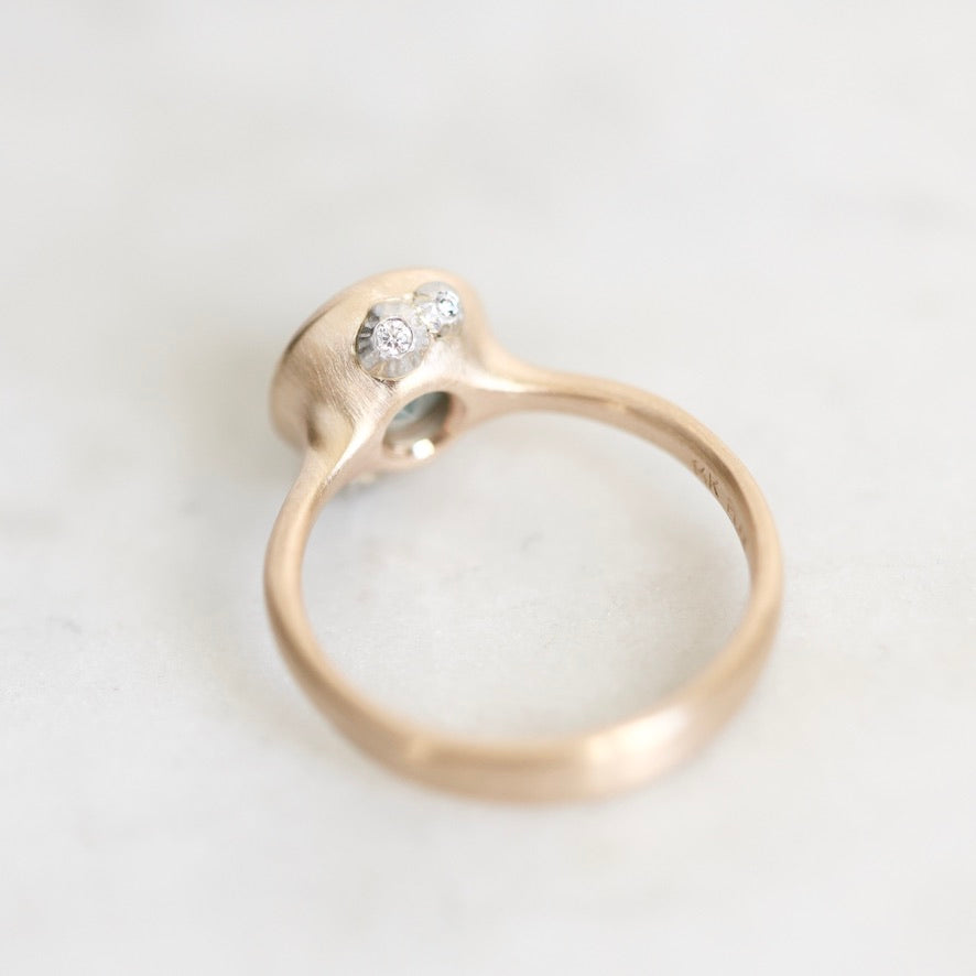A close-up shot of a gold ring with a unique organic-shaped setting featuring small barnacles, resting on a light marble surface.