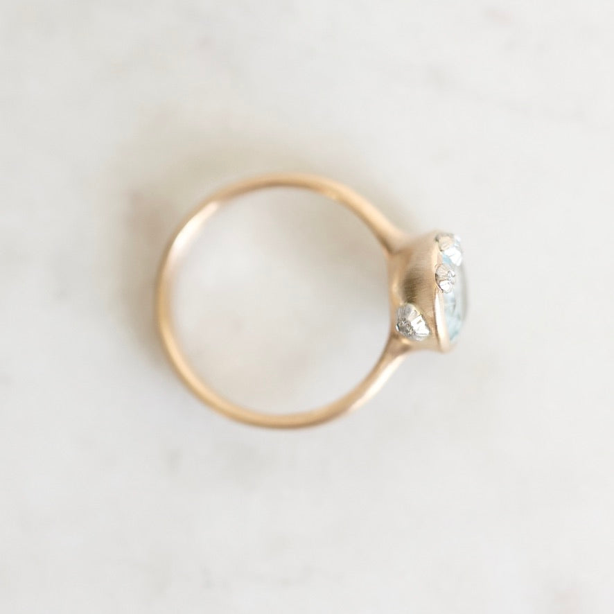 A gold ring with a small gemstones in a bezel setting, photographed from above on a light marble-like surface.