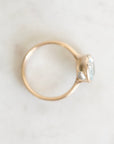 A gold ring with a small gemstones in a bezel setting, photographed from above on a light marble-like surface.