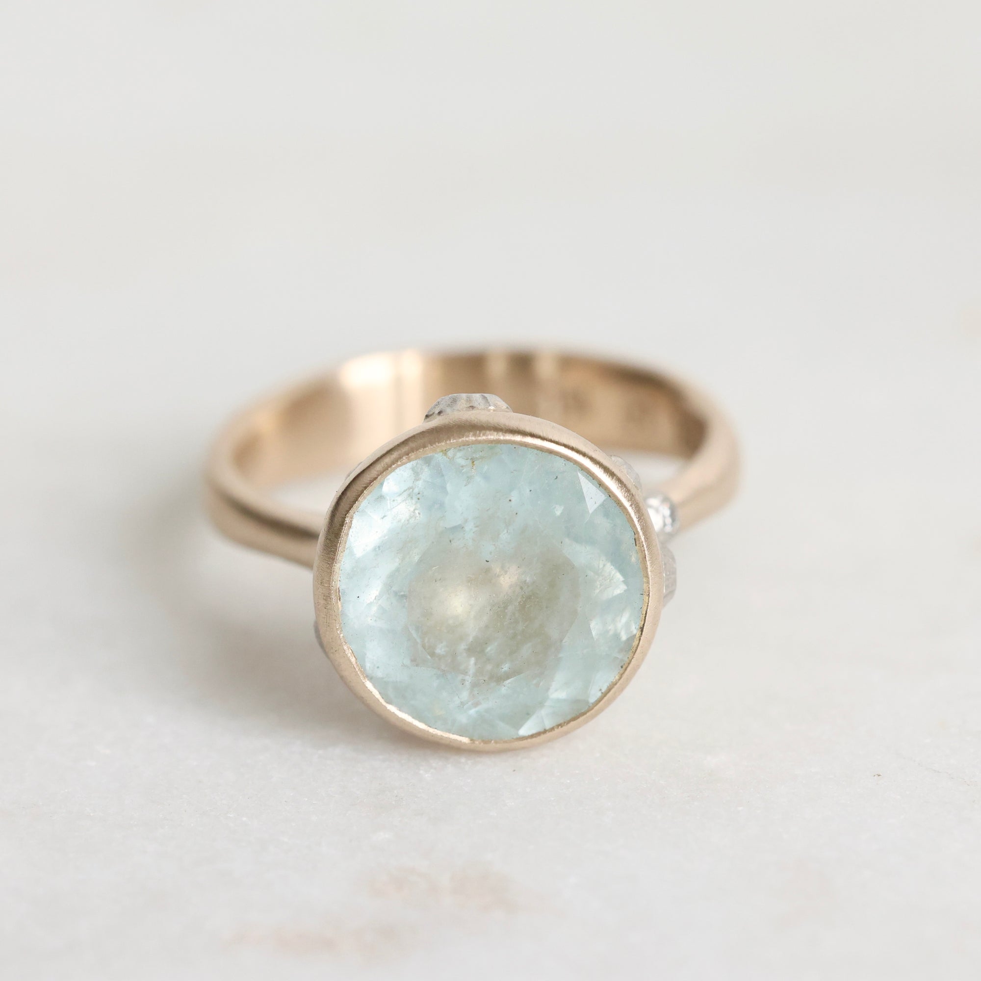 Gold ring with a large, faceted aquamarine stone on a light background