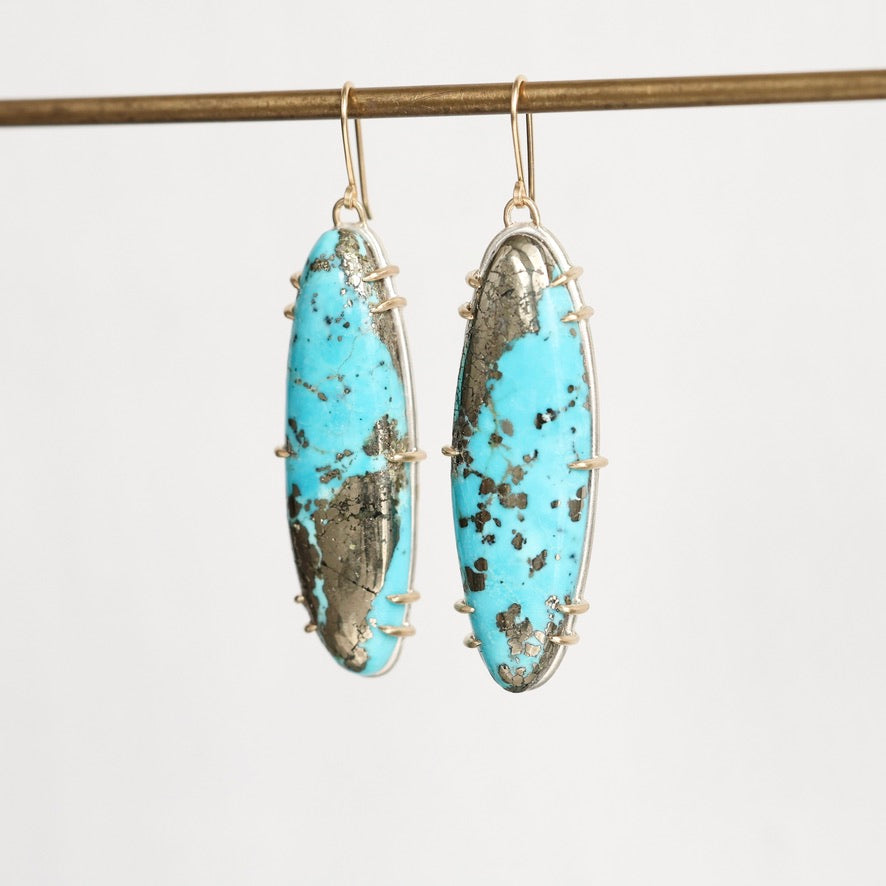 A pair of long oval drop earrings with bright turquoise-blue marbled stone inlays set in silver-toned metal, hanging from gold-toned hooks against a plain light background.