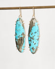 A pair of long oval drop earrings with bright turquoise-blue marbled stone inlays set in silver-toned metal, hanging from gold-toned hooks against a plain light background.