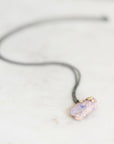 A fossilized opal adorned with gold barnacle details set east west on an oxidized silver chain laid out on a marble background. 
