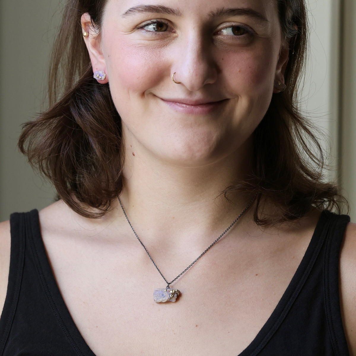 Woman wearing raw opal necklace on an oxidized chain against a plain indoor background. 