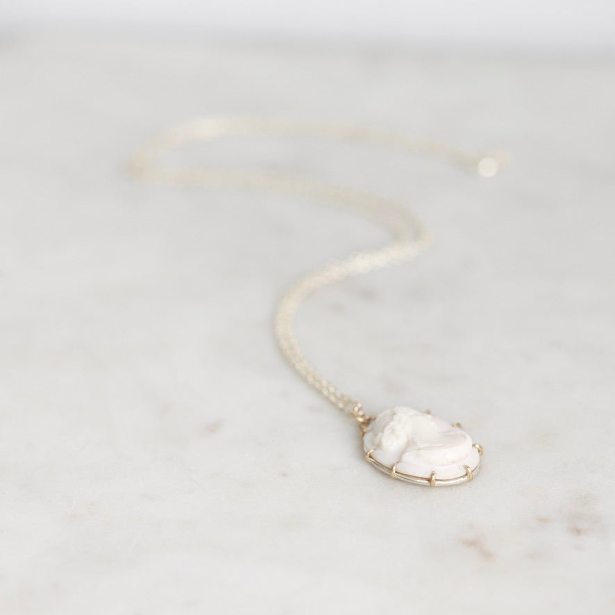 A delicate chain necklace with an oval white carved cameo pendant, resting on a light marble surface.