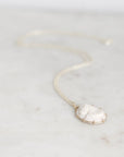 A delicate chain necklace with an oval white carved cameo pendant, resting on a light marble surface.