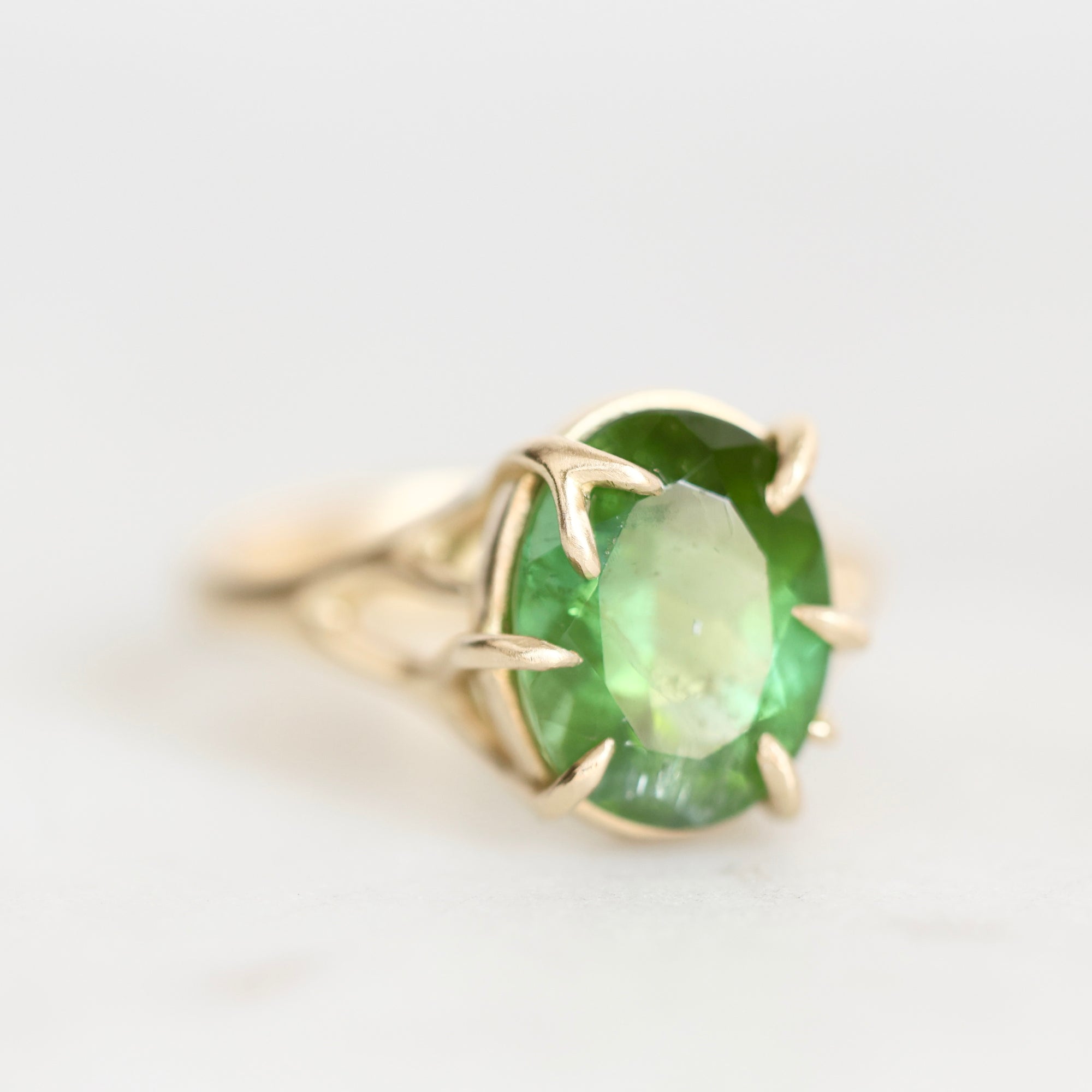 A yellow gold ring featuring an oval-cut green gemstone in a prong setting, photographed on a clean white background.
