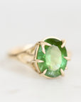 A yellow gold ring featuring an oval-cut green gemstone in a prong setting, photographed on a clean white background.