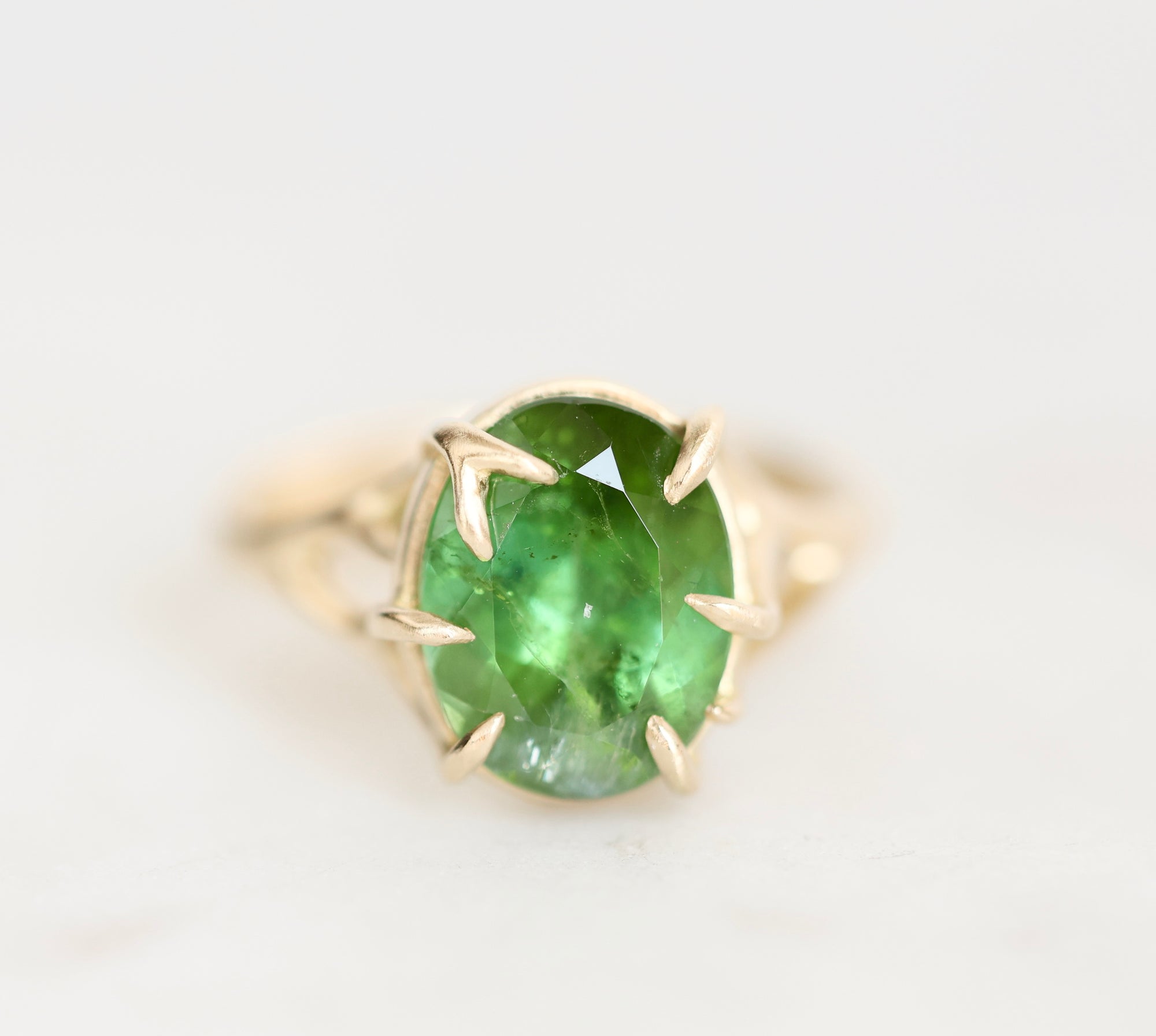 A yellow gold ring featuring an oval-cut green gemstone in a prong setting, shown on a clean white background.