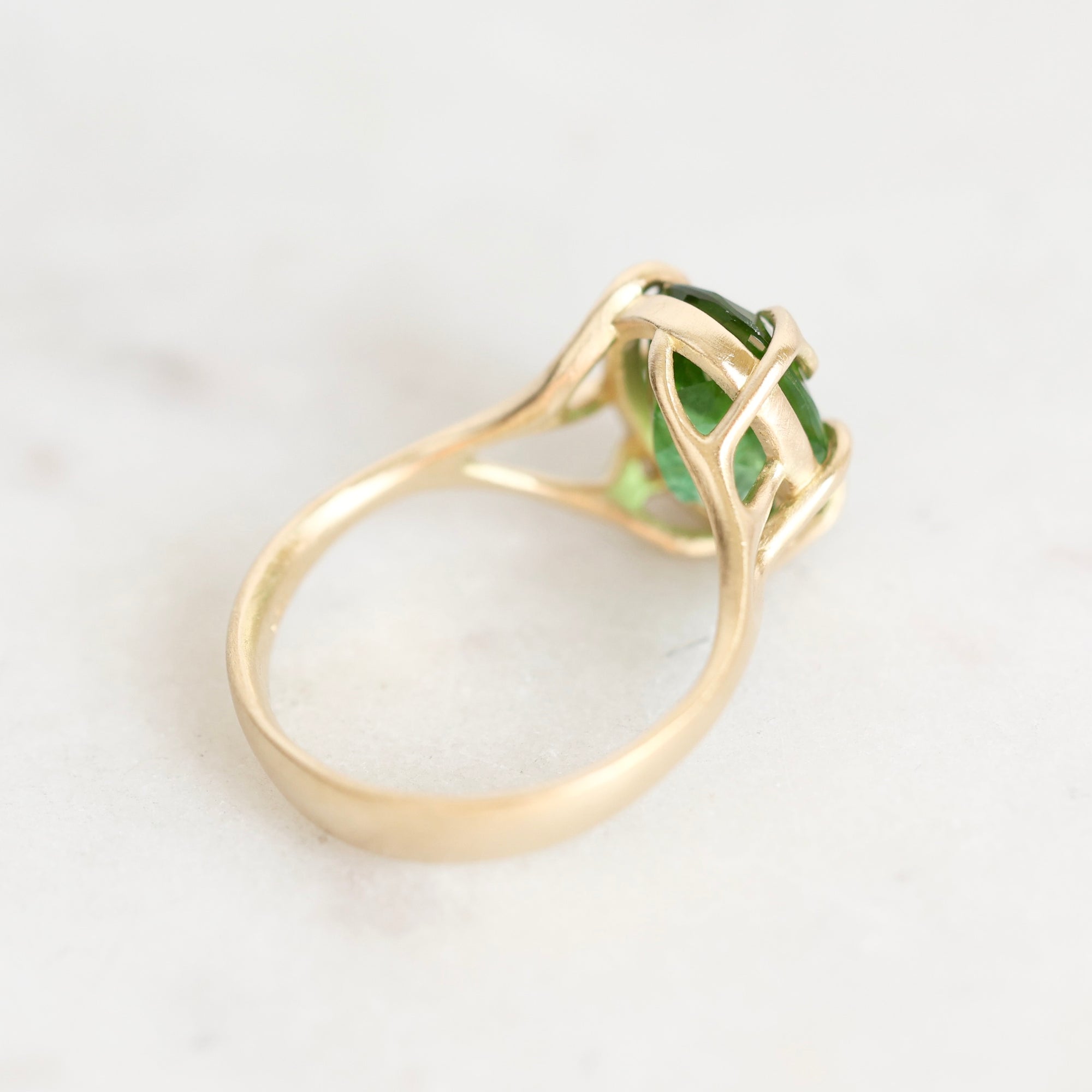 A yellow gold ring with a green gemstone, photographed on a light marble surface.