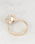 A close-up shot of a vintage yellow gold ring with a cluster of small clear gemstones on the top, set against a light marble background.