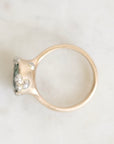 A gold ring with a textured, organic-shaped setting featuring small clear gemstones, photographed from above on a light marble surface.