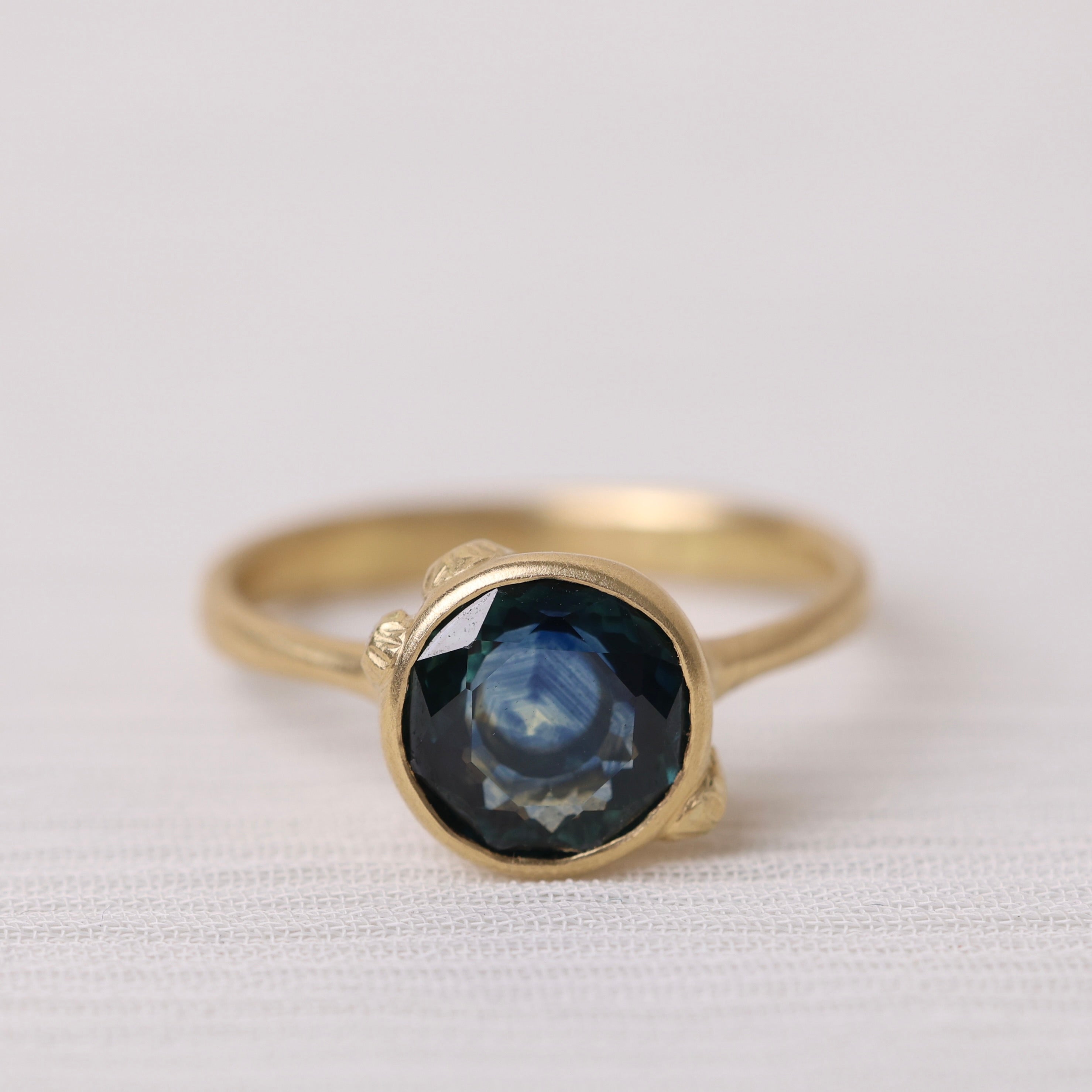 Gold ring with a dark gemstone on a white fabric background
