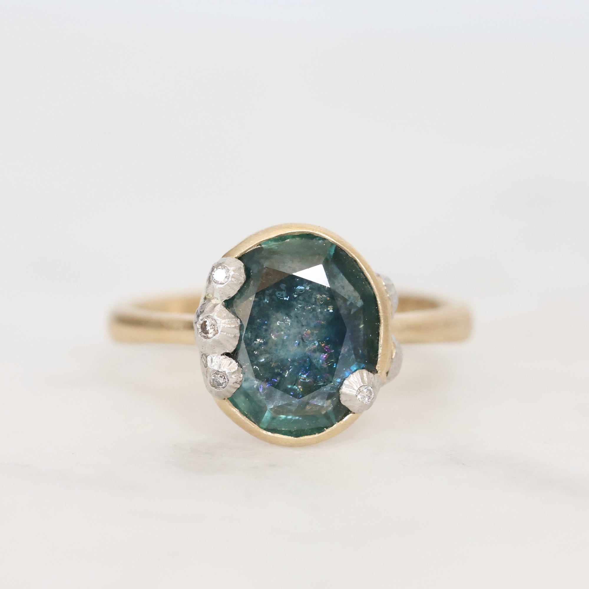 Ring with a blue gemstone and gold setting on a light gray background