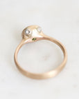 A gold ring with a unique sculptural dome top featuring two clear gemstones and a tiny green accent, photographed on a light marble surface.