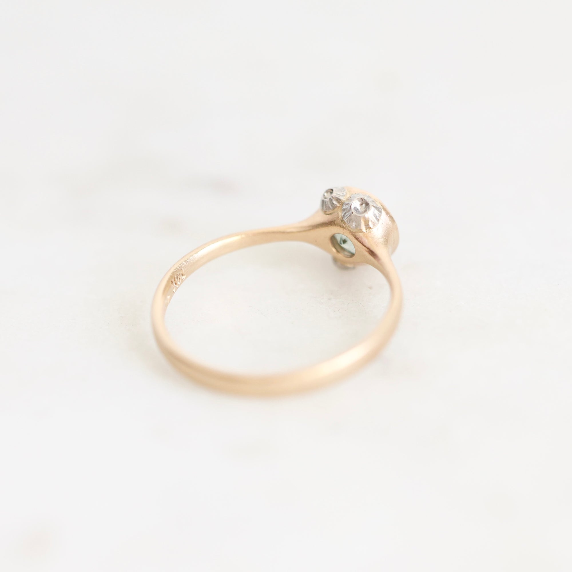 A delicate yellow gold ring with a small cluster of clear gemstones on a polished band, resting on a light off-white marble surface.