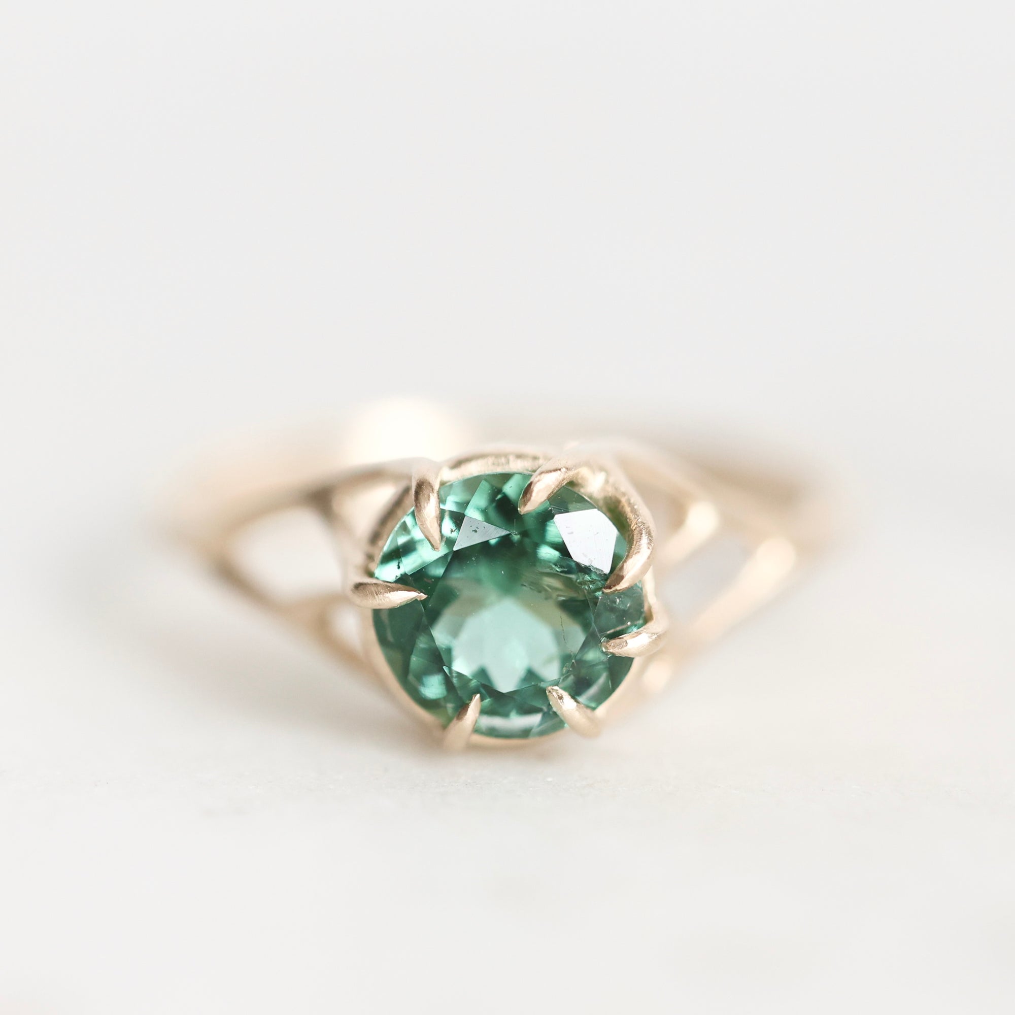 A gold ring featuring a round-cut green gemstone in a prong setting, photographed on a clean white background.