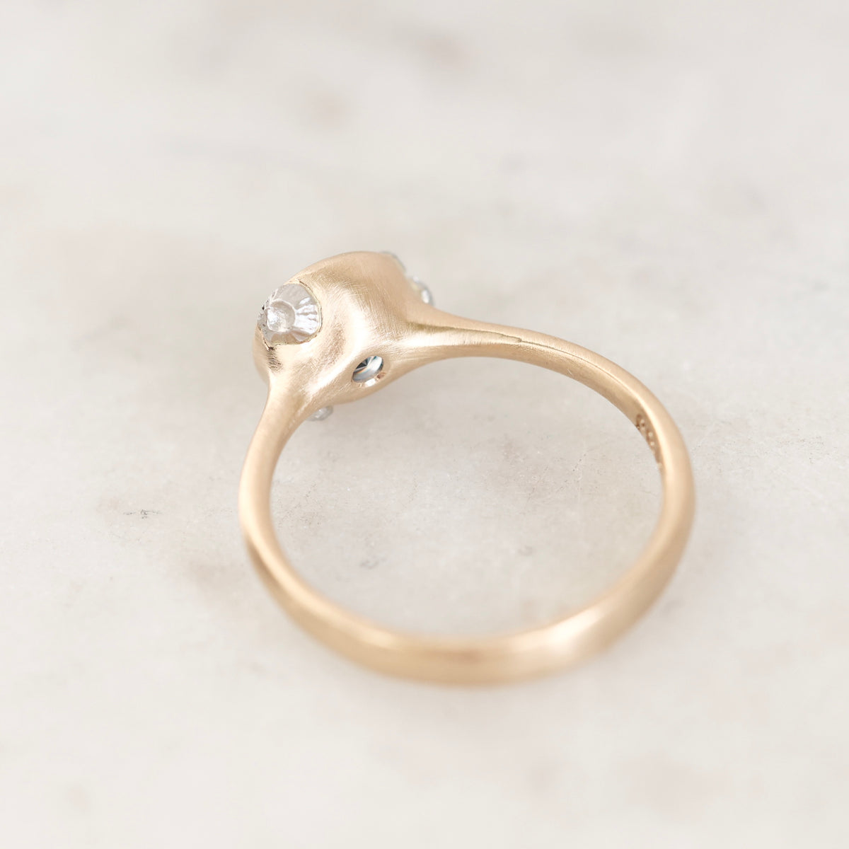 A gold ring with a sculptural, organic-shaped setting and barnacle details resting on a light marble surface.