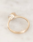A gold ring with a sculptural, organic-shaped setting and barnacle details resting on a light marble surface.