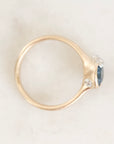 A close-up shot of a gold ring with a blue oval gemstone and two small barnacle details, resting on a light marble surface.