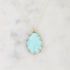 A silver necklace with a teardrop-shaped light blue gemstone pendant, displayed on a white marble surface.