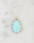 A silver necklace with a teardrop-shaped light blue gemstone pendant, displayed on a white marble surface.