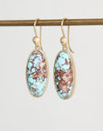 A pair of gold drop earrings with oval turquoise and brown marbled stone inlays, hanging from a gold rod against a light gray background.