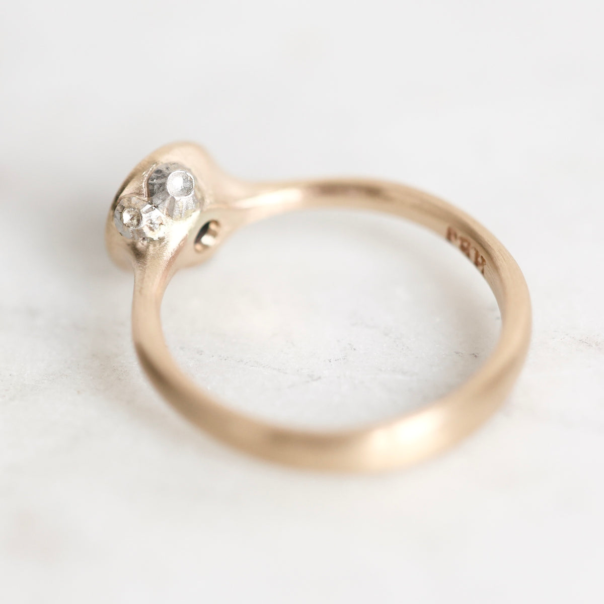 A close-up shot of a vintage rose gold ring with a cluster of small clear stones, resting on a light, textured white surface.