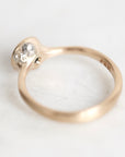 A close-up shot of a vintage rose gold ring with a cluster of small clear stones, resting on a light, textured white surface.