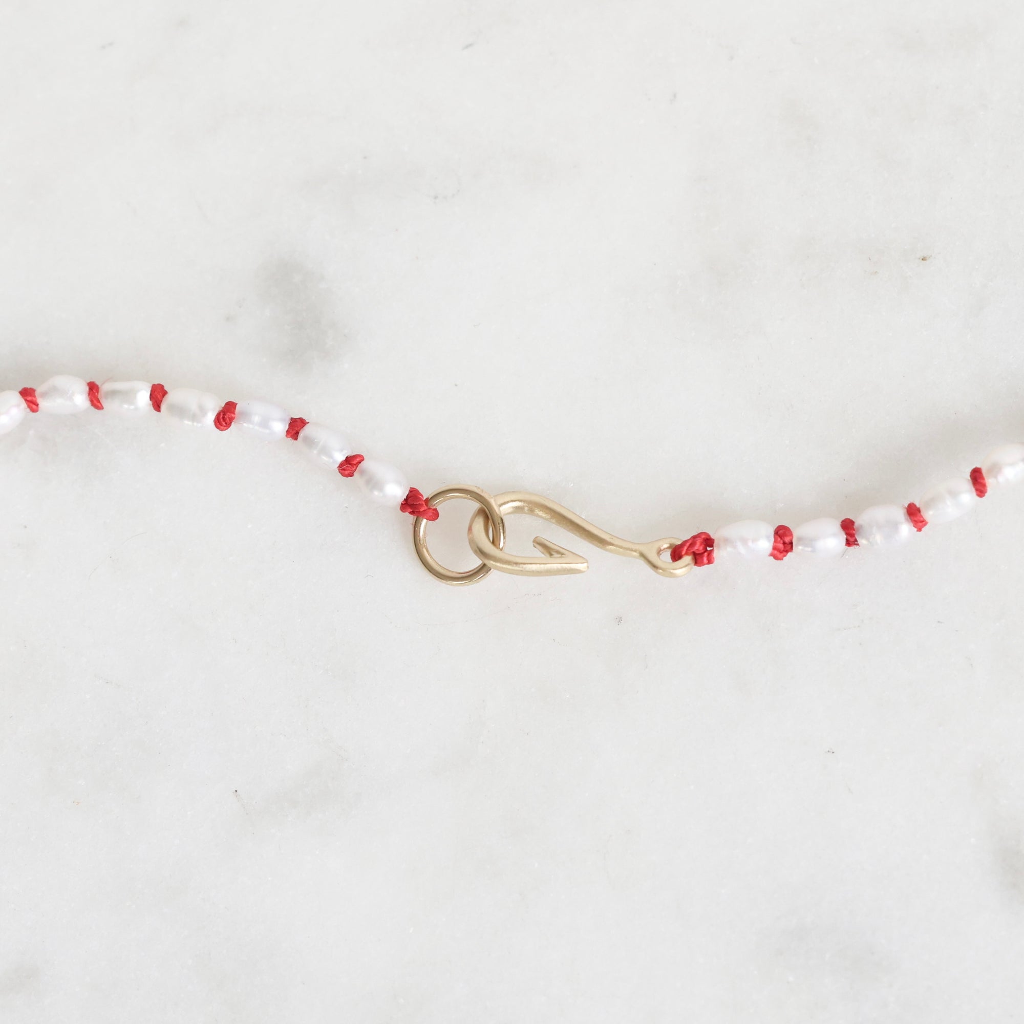 Beaded necklace with red and white beads and a gold clasp on a light gray background
