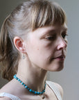 Woman wearing a blue beaded necklace with a neutral background