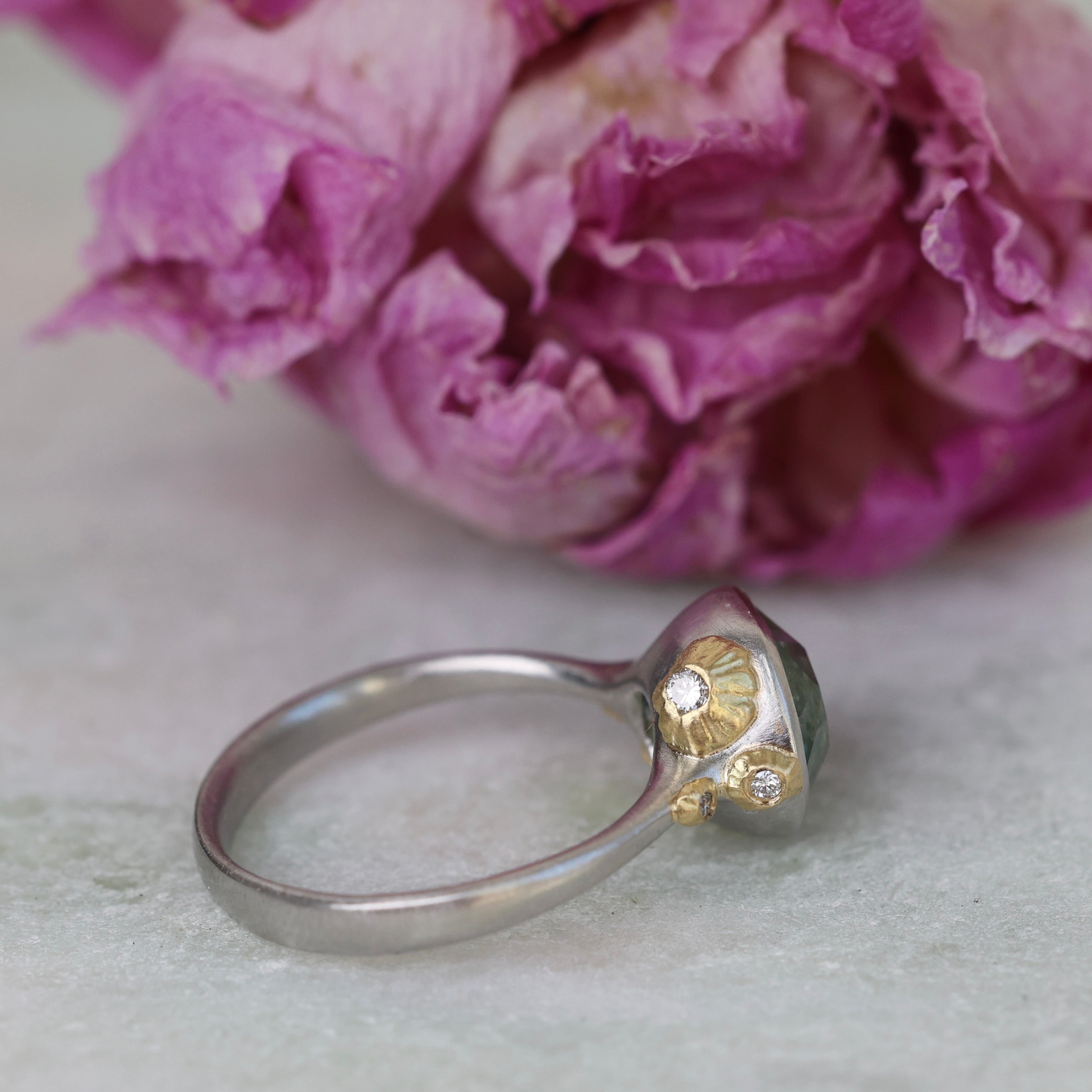 Silver ring with gold accents and Montana sapphire in front of pink flowers