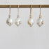 Four pearl drop earrings hanging from a gold-toned rod against a light gray background. Two earrings have white freshwater pearls with small silver floral accents, and two have white pearls with small gold floral accents.