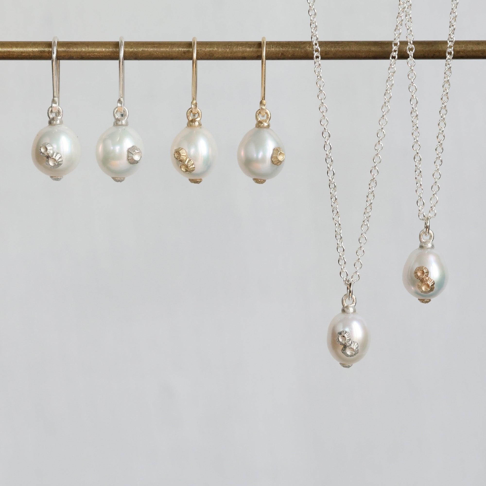 A jewelry set featuring white freshwater pearls with small gold and clear crystal accents, displayed on a gold-colored rod with matching drop earrings and necklaces.