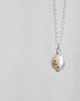 A silver chain necklace with a teardrop-shaped white pearl pendant featuring a textured gold accent on the side, shown against a plain light gray background.