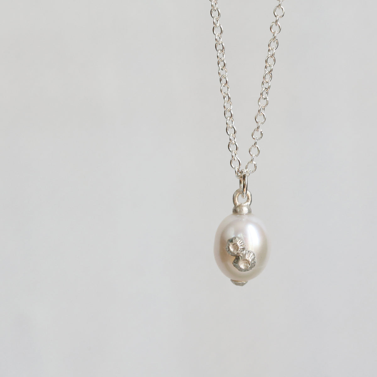A silver chain necklace with a white freshwater pearl pendant featuring a small silver floral accent, shown against a plain light gray background.