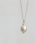 A silver chain necklace with a white freshwater pearl pendant featuring a small silver floral accent, shown against a plain light gray background.