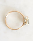 A gold ring with a small cluster of clear gemstones on the setting, photographed from above on a light off-white marble surface.