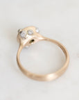A close-up shot of a gold ring featuring a unique organic-shaped setting with three small clear gemstones, photographed on a light, neutral background.