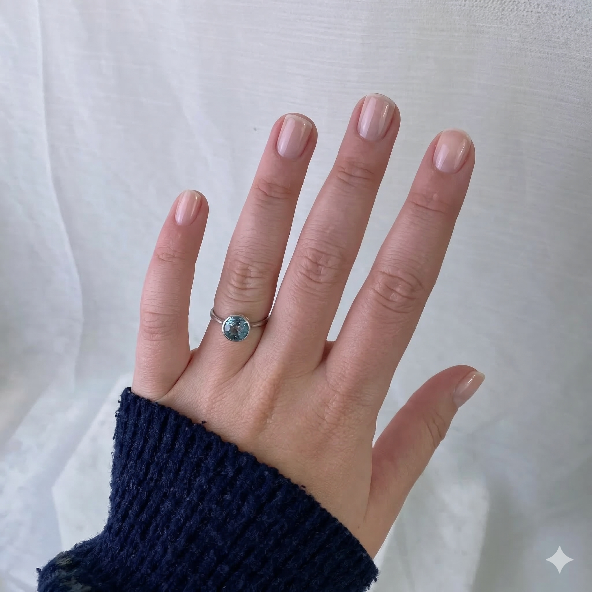 Hand wearing a ring with a blue gemstone against a white background