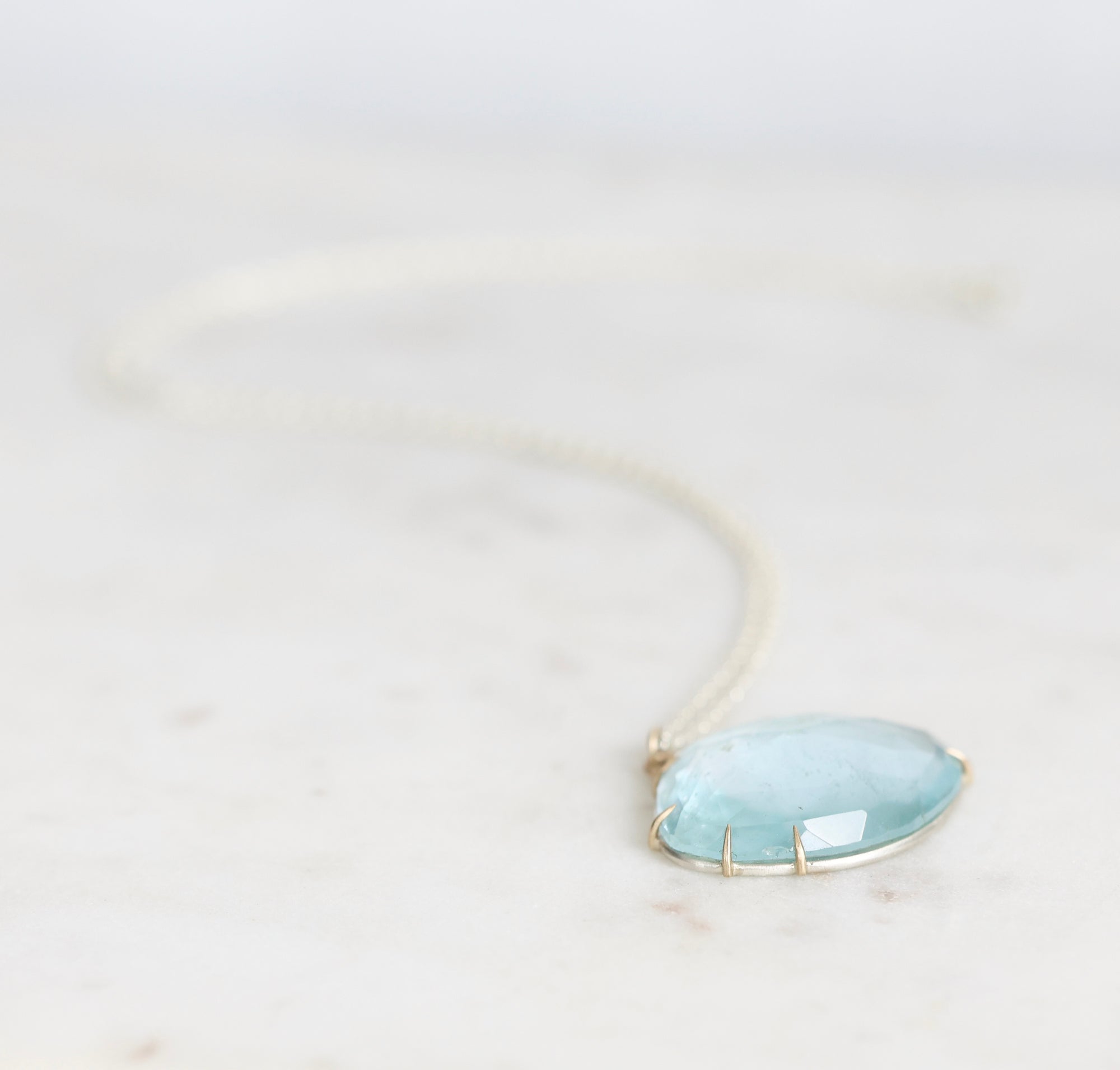 Blue topaz necklace laid out on marble with gold prongs