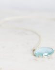 Blue topaz necklace laid out on marble with gold prongs