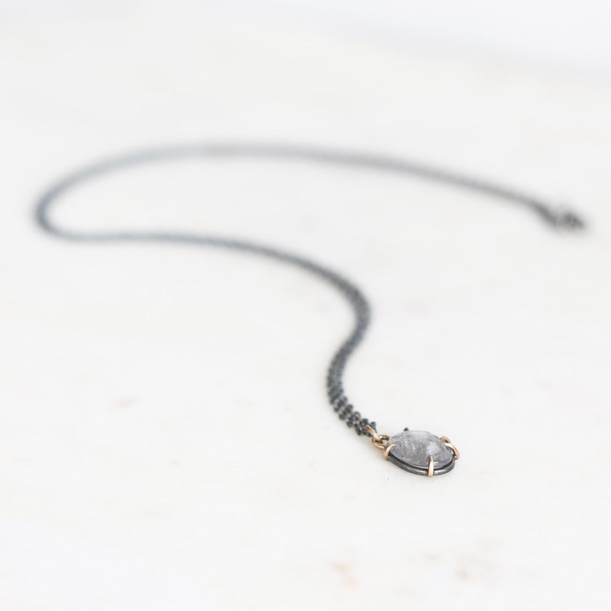 Purple spinel necklace with oxidized chain laying on marble surface