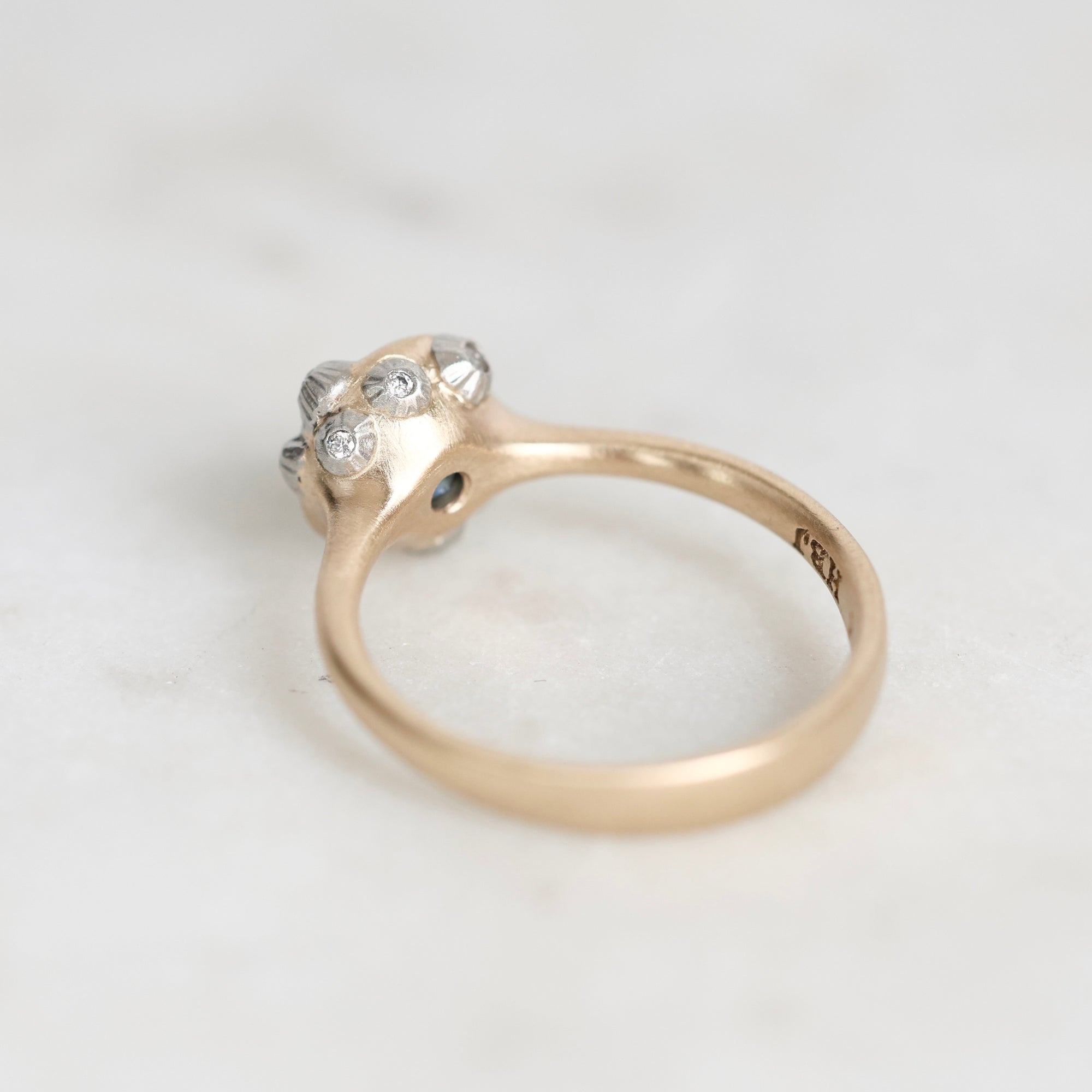 A vintage-style gold ring with a cluster of small barnacles on the setting, photographed on a light marble surface. 