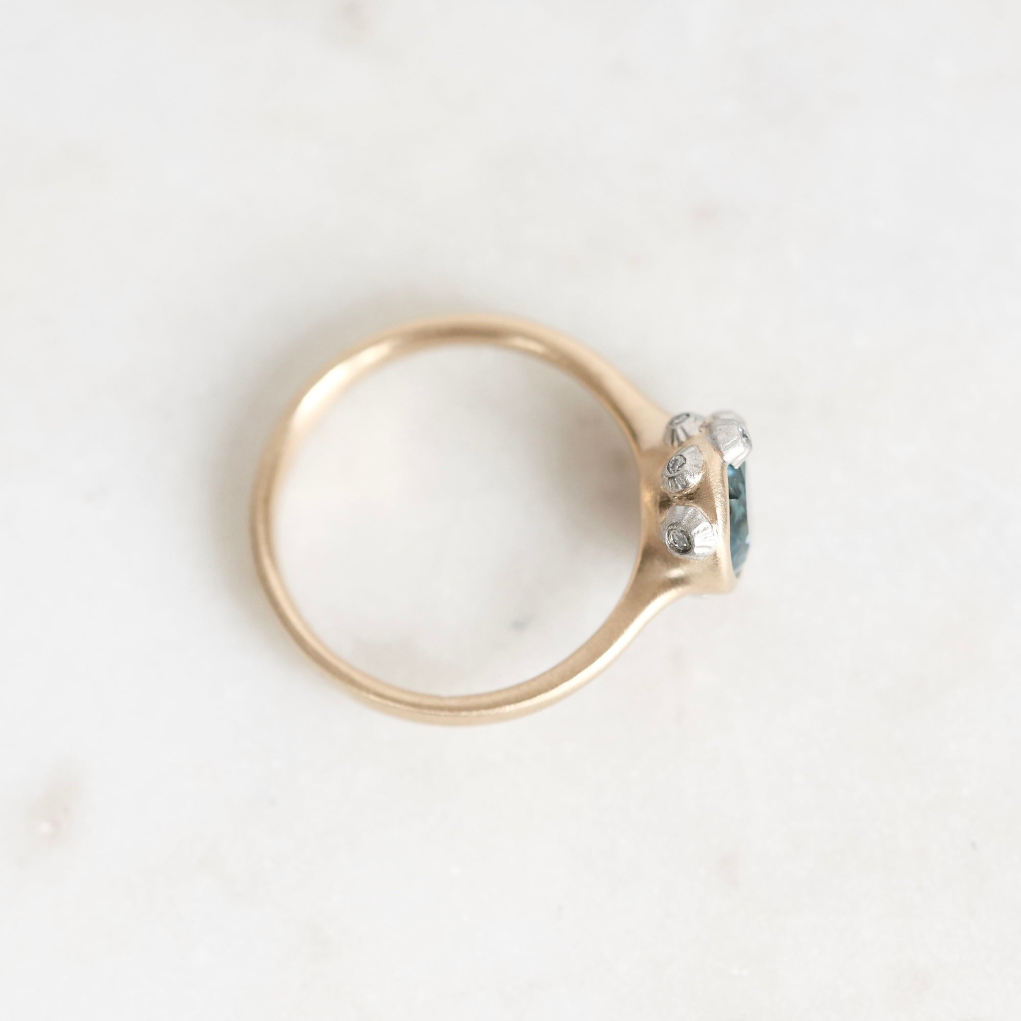 A gold ring with a small cluster of clear gemstones on the side, photographed on a light marble-like surface.