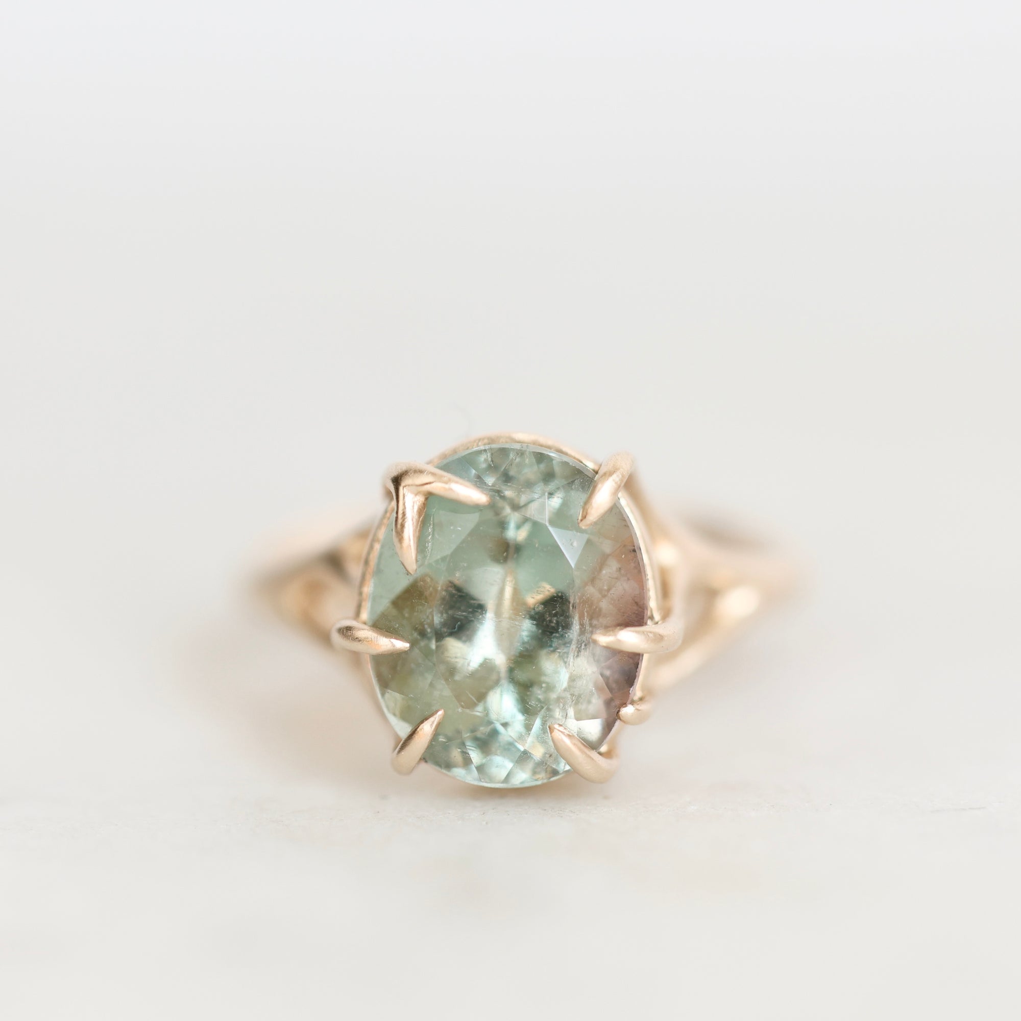 A round-cut light blue-green gemstone ring in a gold prong setting, photographed on a clean white background.