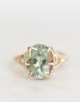 A round-cut light blue-green gemstone ring in a gold prong setting, photographed on a clean white background.