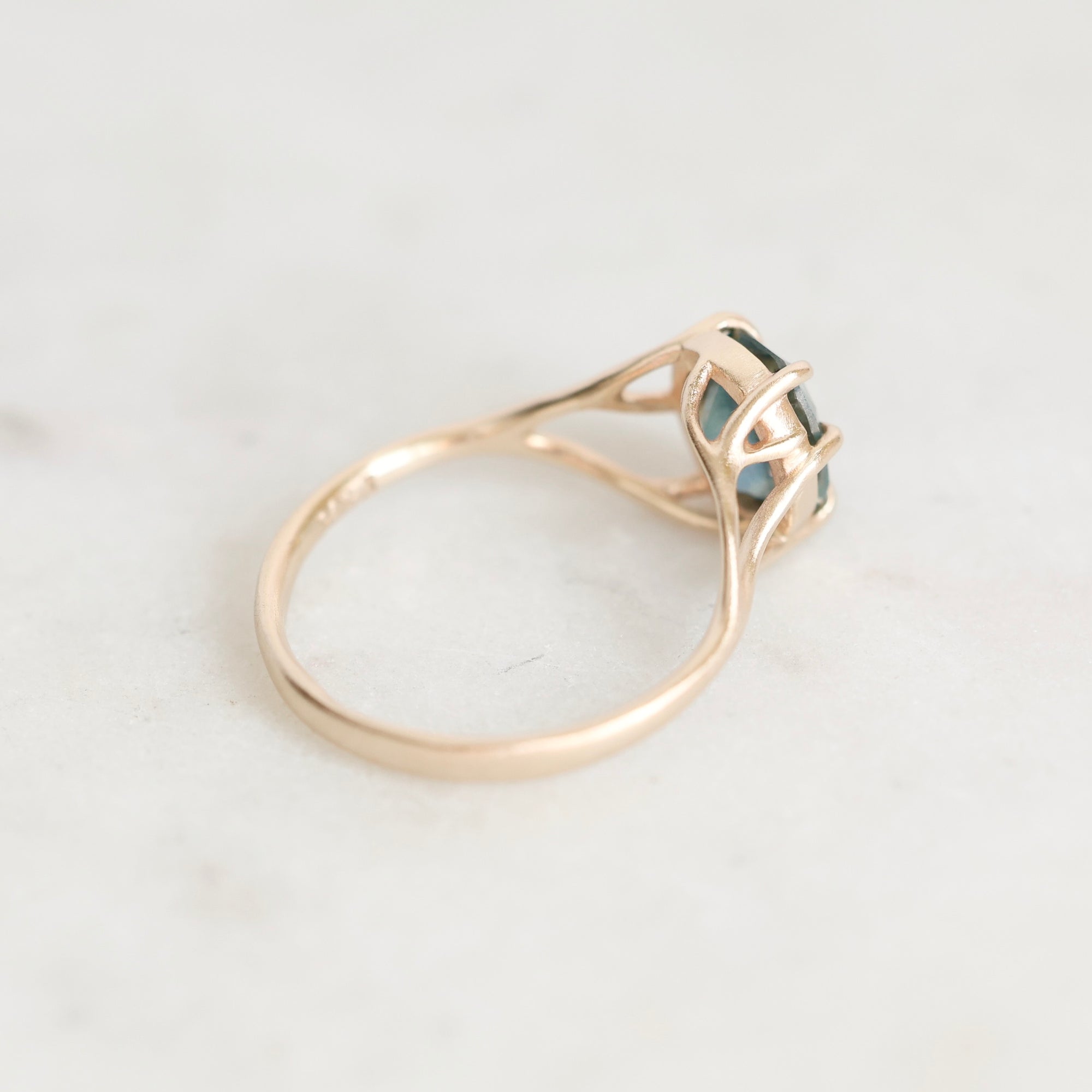 A rose gold ring with a small dark green gemstone, photographed on a light marble surface.